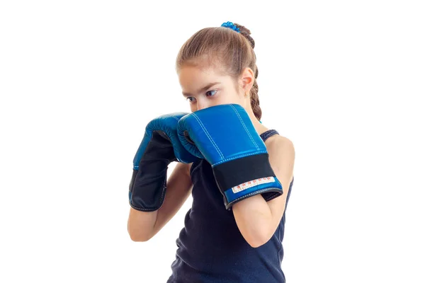 Little girl with pigtail stands in the large blue boxing gloves in front of a camera — Stock Photo, Image