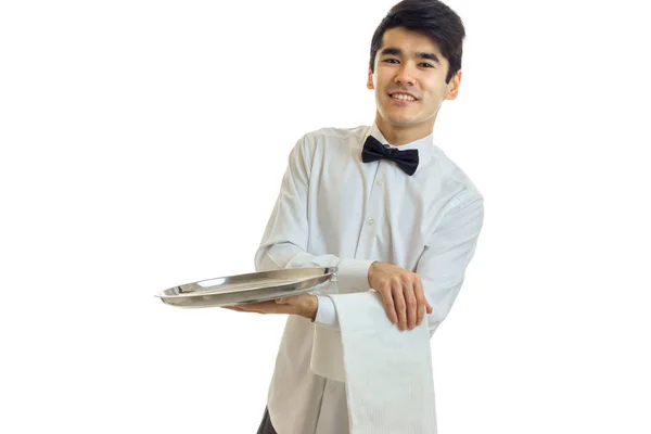 Perky young waiter in a white shirt with black bow tie holding a towel and tray for dishware — Stock Photo, Image