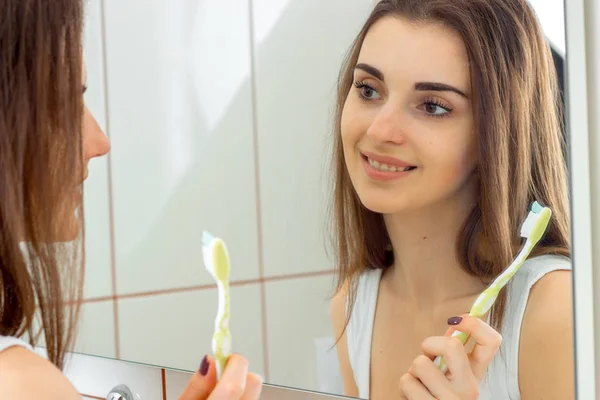 Усміхнена молода дівчина стоїть перед дзеркалом з зубною щіткою — стокове фото