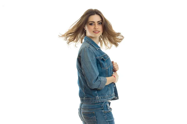 Hermosa joven en traje de jeans se para de lado y sonriendo —  Fotos de Stock