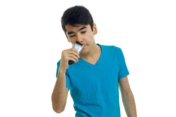 Young brunette in a blue t-shirt shaves shaving machine face — Stock Photo, Image