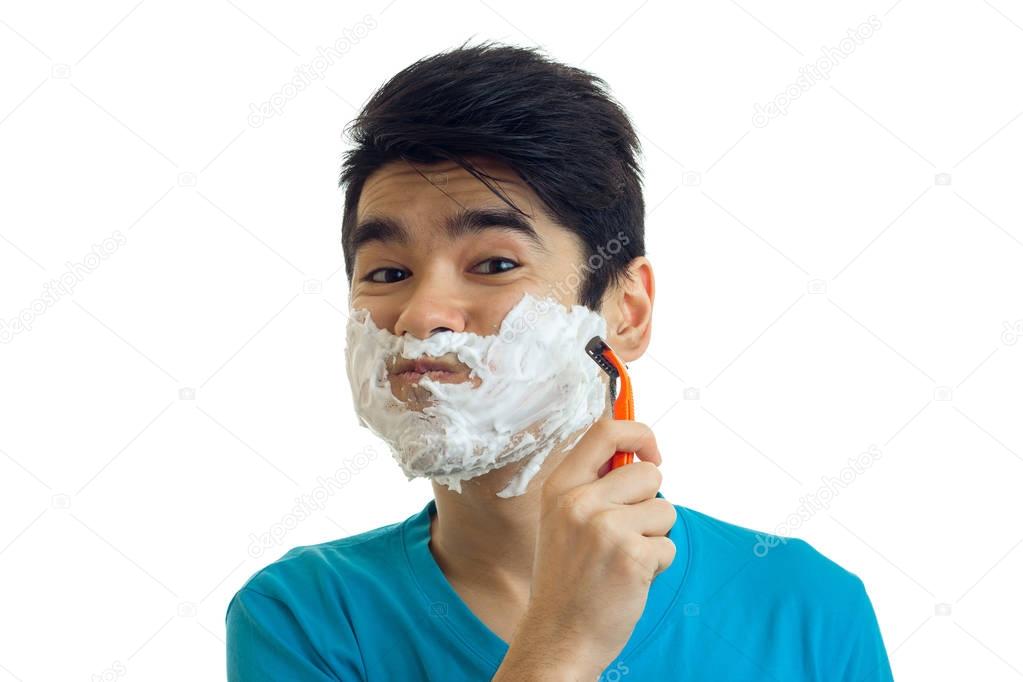 Portrait of a cheerful young man with foam on his face who shaves his beard machine close-up