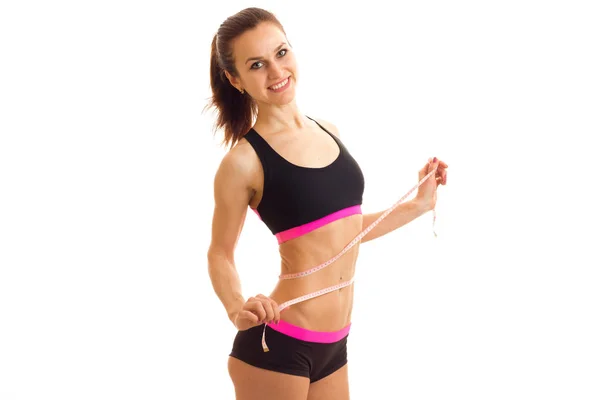 Smiling sports girl in top and shorts takes the waist measuring tape — Stock Photo, Image