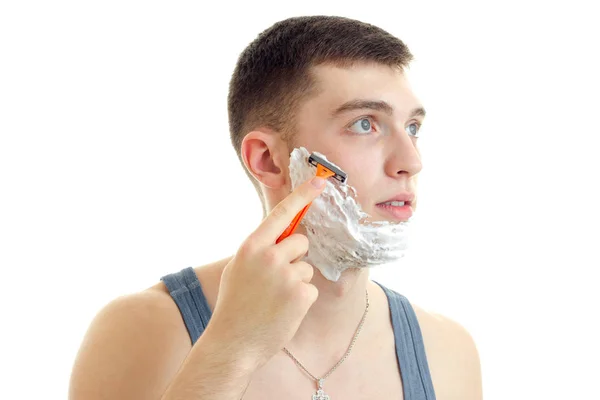 Joven mira hacia otro lado y se afeita la barba con una navaja de afeitar de cerca —  Fotos de Stock