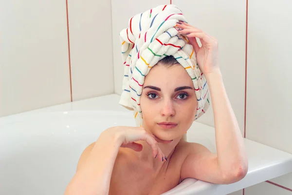 Piękna młoda dziewczyna z ręcznikiem na włosach leży w łazience i wygląda prosto — Zdjęcie stockowe