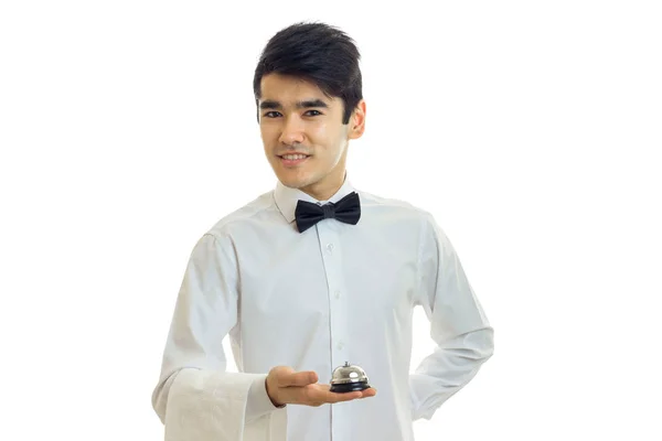 Aantrekkelijke jonge ober met ' bow-tie en wit shirt houden een Bell en glimlachen — Stockfoto