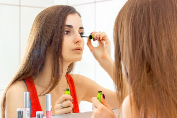En ung vacker flicka ser ut i spegeln och måla ögonfransar — Stockfoto