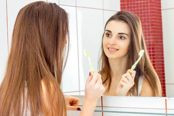 Веселая молодая девушка стоит перед зеркалом и держит зубную щетку — стоковое фото