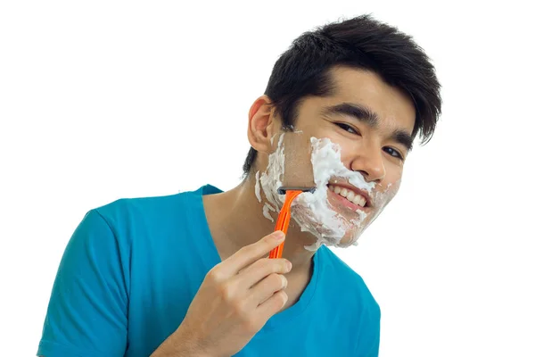 Hermoso chico sonriente con espuma en su cara mira a la cámara y se afeita la máquina de barba Fotos de stock libres de derechos