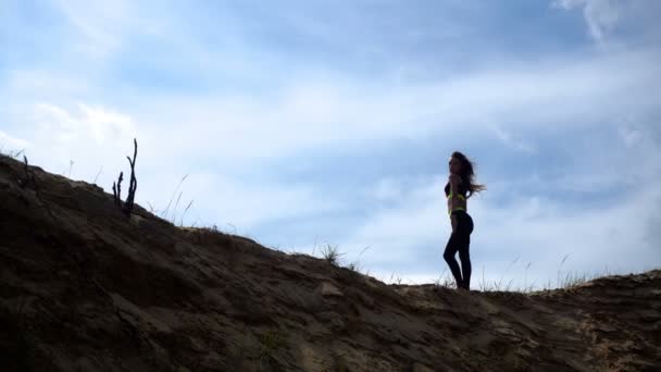 Fille de sport se tient sur une colline de sable — Video