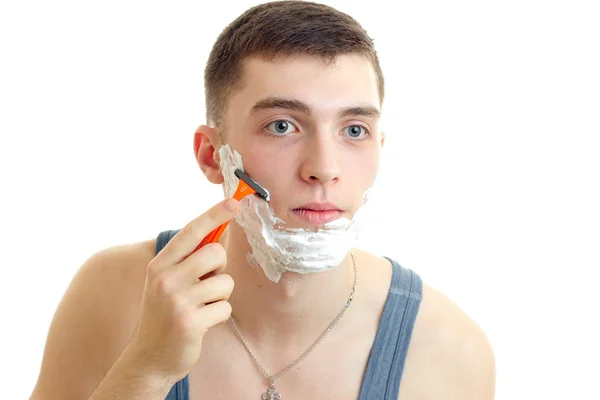 Jovem cara olha em frente e barba sua barba com uma navalha com espuma — Fotografia de Stock