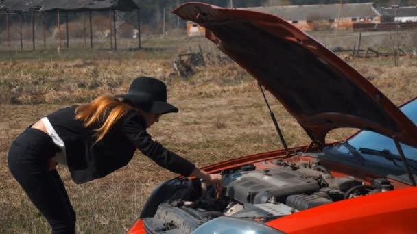 Elegantes Mädchen sieht unter der Motorhaube eines kaputten Autos aus — Stockvideo