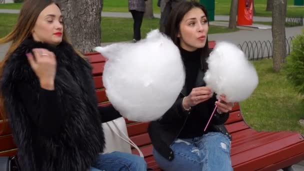Fidanzata sedersi su una panchina e mangiare zucchero filato nel parco — Video Stock