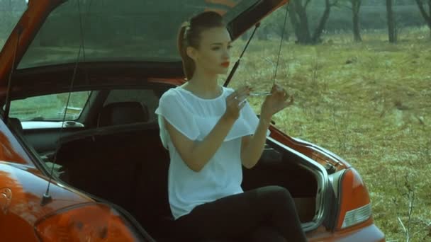 Charmig tjej i solglasögon sitter i bagageluckan på en bil — Stockvideo