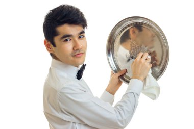 Beyaz gömlekli büyüleyici genç garson kameraya bakar ve yakın çekim için havlu tepsisini losyonları