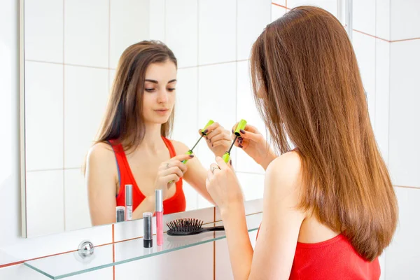 Söt ung tjej med vackra hår står framför spegeln och måla läpparna — Stockfoto