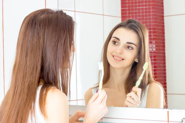 Радісна молода дівчина стоїть перед дзеркалом і тримає в руці зубну щітку — стокове фото