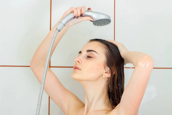 Beautiful young girl stands under the shower closing her eyes and washes her head — Stockfoto