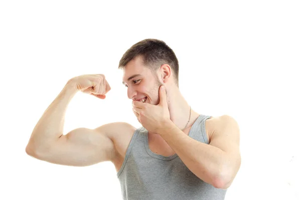 Sporty young guy looks on the muscles in the arm and smiling close-up — Stock Photo, Image