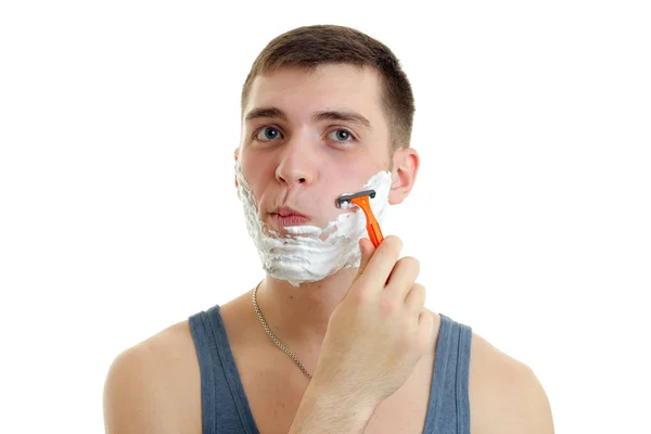 Retrato de um rapaz ridiculamente jovem com espuma no rosto que rapa a máquina da barba — Fotografia de Stock