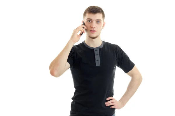 Чарівний молодий чоловік у чорній футболці дивиться прямо і тримає мобільний телефон біля вашого вуха — стокове фото