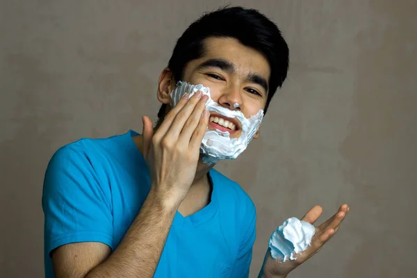 Bel ragazzo sorridente con i capelli neri sta causando la schiuma per barba primo piano — Foto Stock