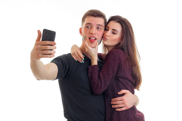 Vacker flicka pussar på kinden av en ung attraktiv kille och han gör selfi på telefon — Stockfoto