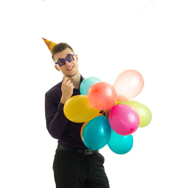 Jovem maravilhoso com um cone na cabeça mantém perto do rosto óculos de papel balões e sorrindo — Fotografia de Stock
