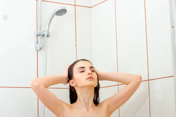 Joven hermosa chica está de pie bajo la ducha cerrando los ojos y se lava las manos pelo —  Fotos de Stock