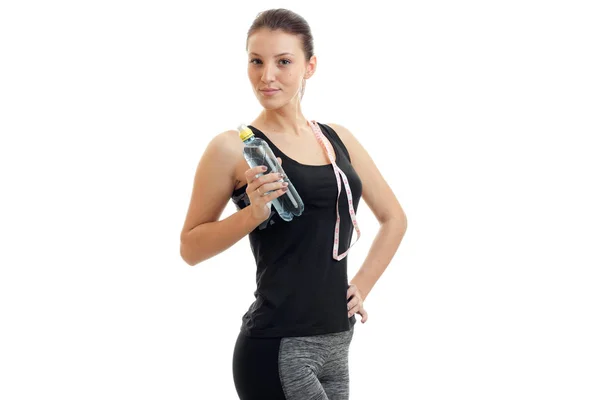 Cute young girl in fitness black t-shirt looks away and keeps the shoulder strap and a bottle of water in hand — Stock Photo, Image