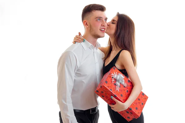 Linda chica joven sosteniendo un regalo y besa al chico guapo sonriendo — Foto de Stock