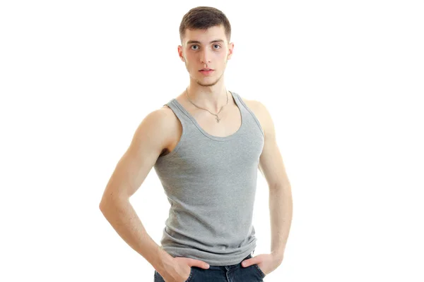 Handsome young guy standing in a t-shirt and keeps his hands in his pockets — Stock Photo, Image