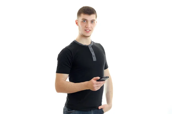 Alegre guapo chico en un negro camiseta sosteniendo un teléfono y mirando directamente — Foto de Stock