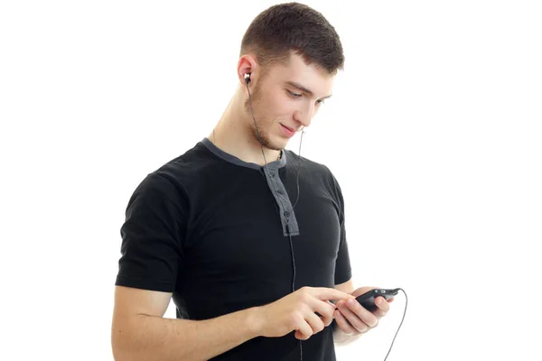 Charmante jonge kerel in de zwarte shirt ziet er in close-up van de mobiele telefoon — Stockfoto