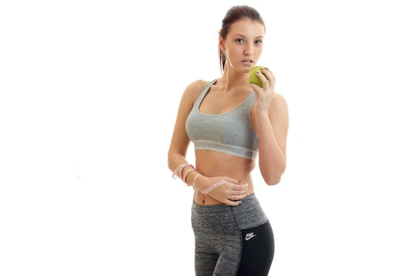 Great athletic girl stands in fitness suit and eats Green Apple — Stock Photo, Image
