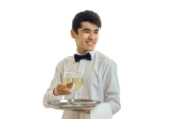 Hilarante lindo joven camarero mira hacia otro lado riendo y sosteniendo copas de vino en una bandeja que — Foto de Stock