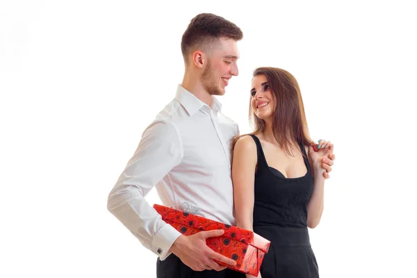 Uma jovem encantadora em um vestido e olhando para o cara bonito na camisa e com um presente na mão — Fotografia de Stock