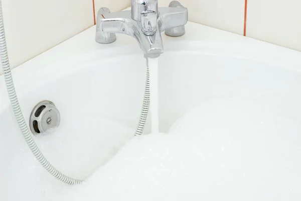 Вода, которая плавает из крана в ванной комнате с пеной — стоковое фото