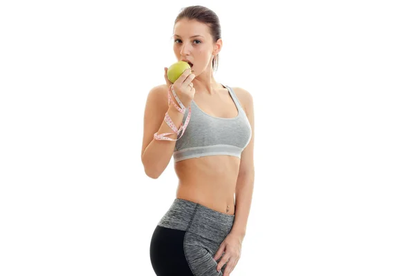 可爱的年轻健身女孩灰色顶部侧身站立和吃青苹果 — 图库照片