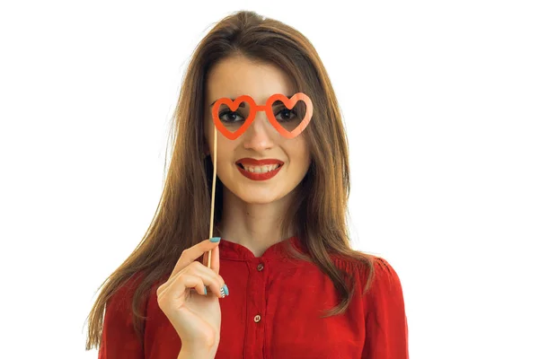Young charming wonderful girl laughs and keeps near eye red paper glasses — Stock Photo, Image