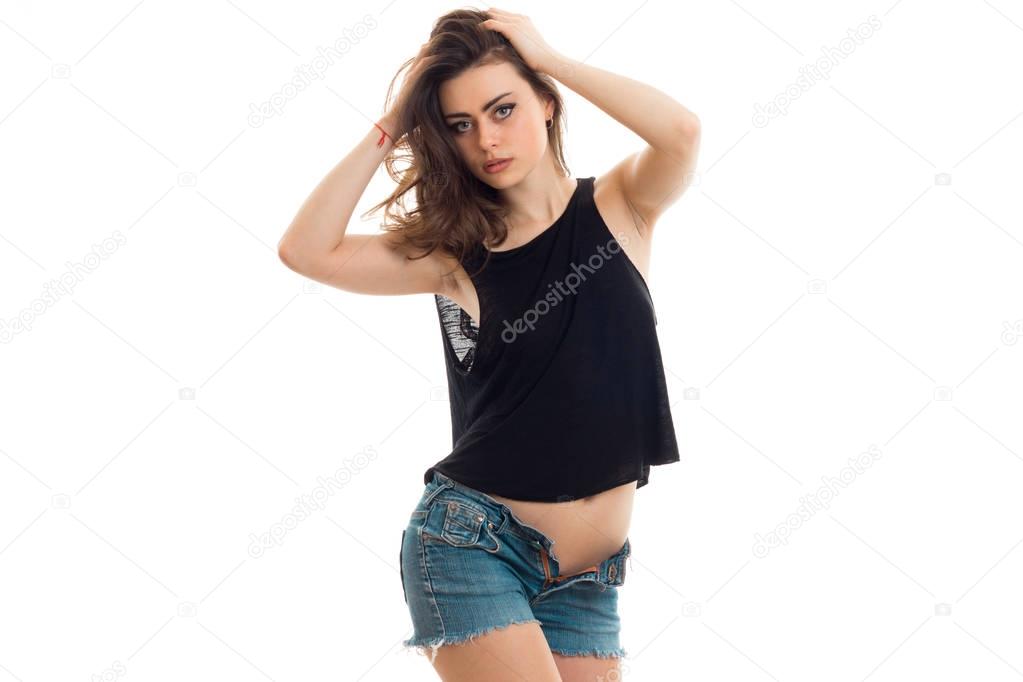 attractive young girl in t-shirt and shorts keeps hands hair and sexy looking at camera