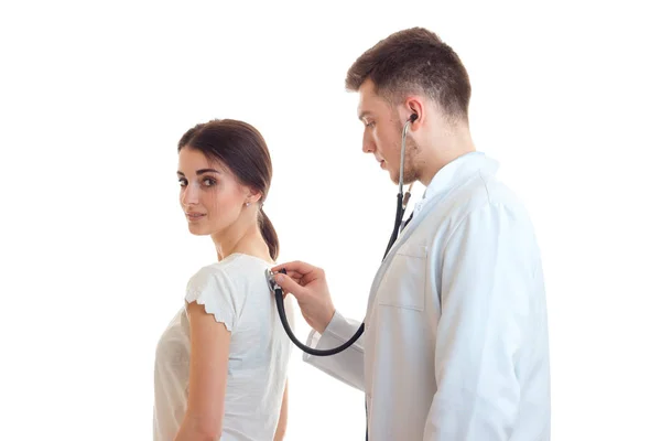 Un médico joven con una bata blanca de laboratorio con un estetoscopio está escuchando a la niña de cerca —  Fotos de Stock