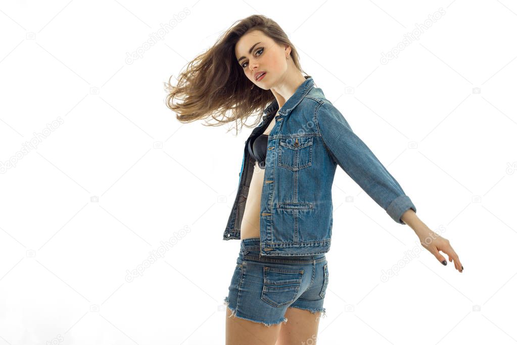 great young brunette with beautiful developing hair in a jeans suit, keeping her hand in the face and looks at the camera