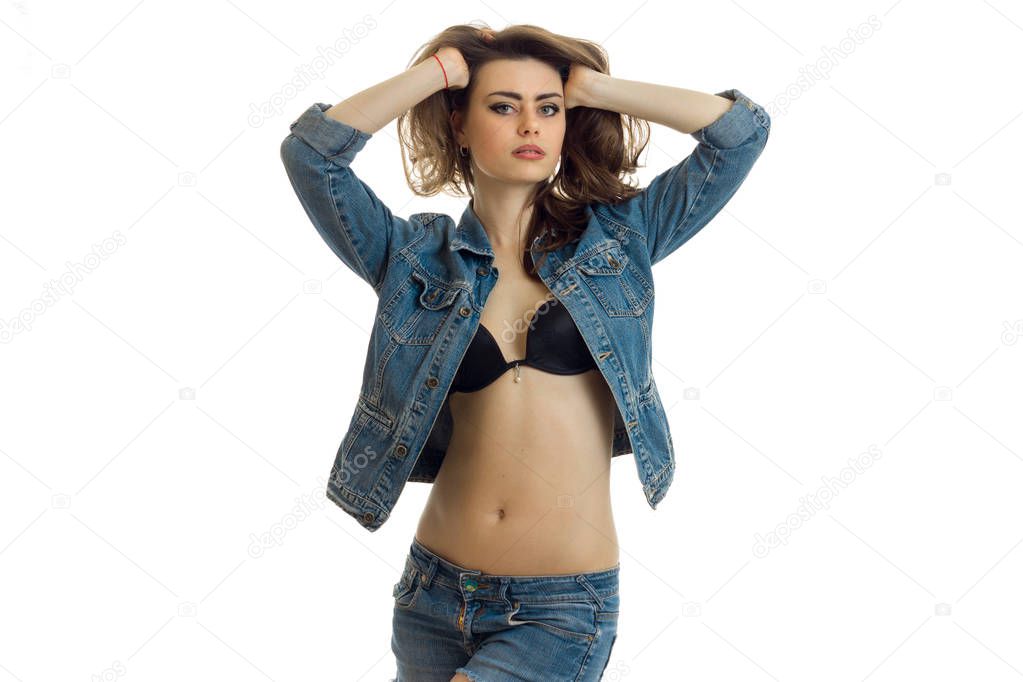 sexy young girl in black bra and with unfastened denim jacket keeps hands and hair looks straight