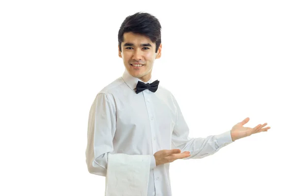 Atraktivní mladý číšník úsměvy udržuje ubrousek a drží ruku směrem k — Stock fotografie