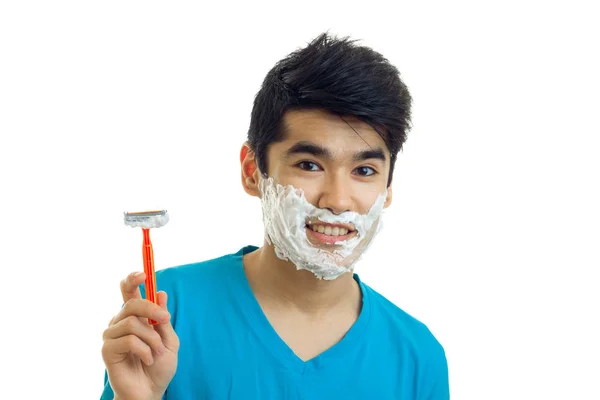 L'affascinante ragazzo sorridente con la schiuma sul viso sorridente e con una macchina da barba in mano — Foto Stock