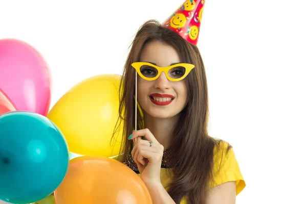 Портрет красивой молодой девушки, которая улыбается и держит возле лица бумажные очки с шариками — стоковое фото