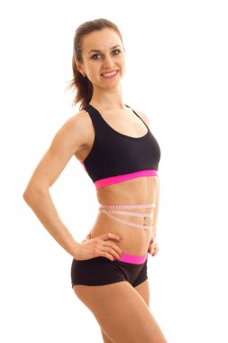 Elini yan bant bel tutar, ölçme ve gülümseyen ince atletik kız