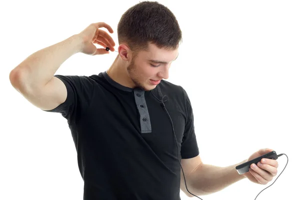 Sporty young man in a black t-shirt holding a phone and listening to music with headphones — Stock Photo, Image