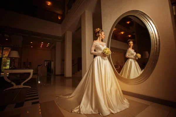 Young bride in wedding dress looking at a big mirror — Stock Photo, Image